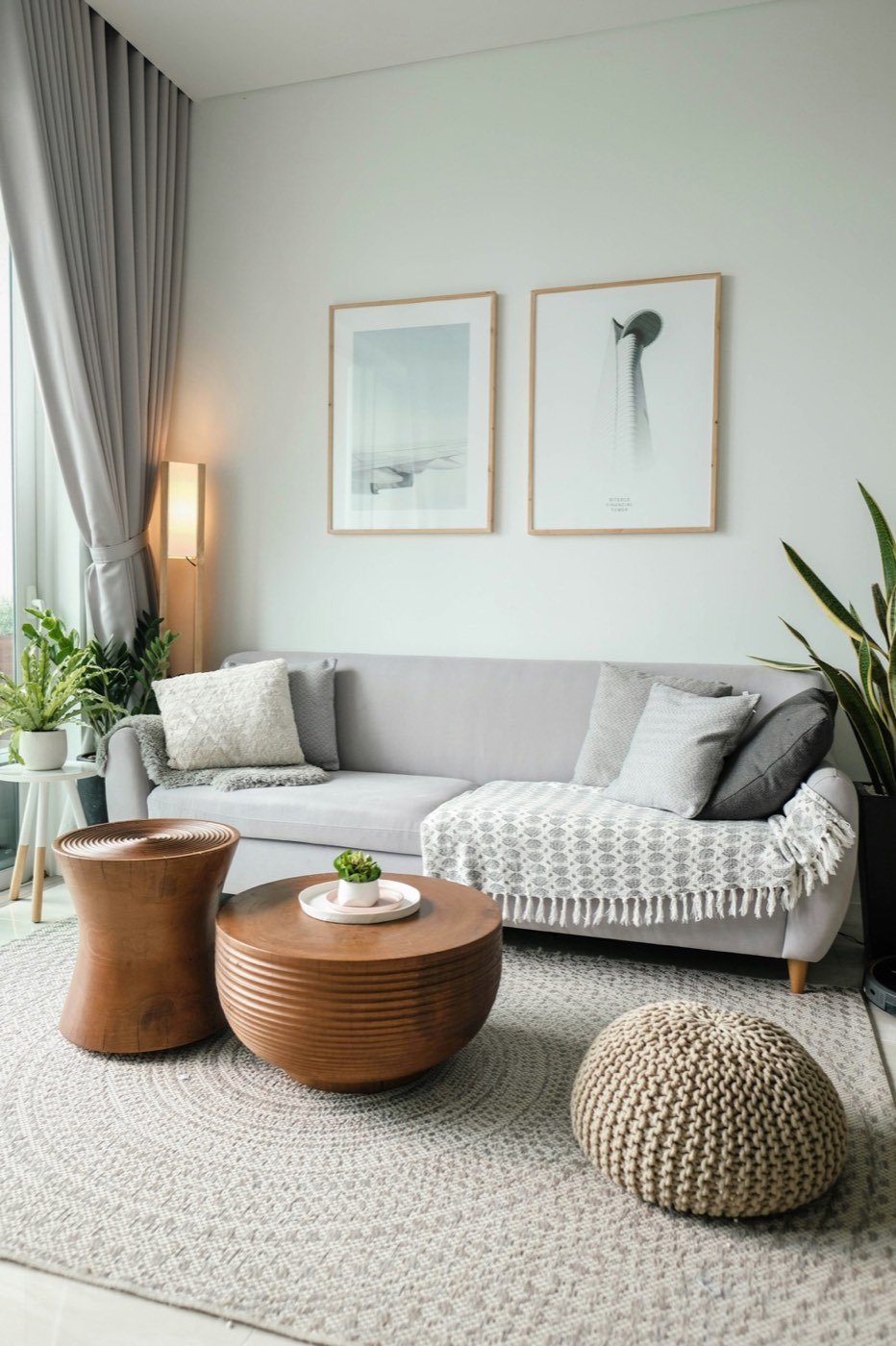 A bright living room with a gray sofa, a woven pouf and a tall window