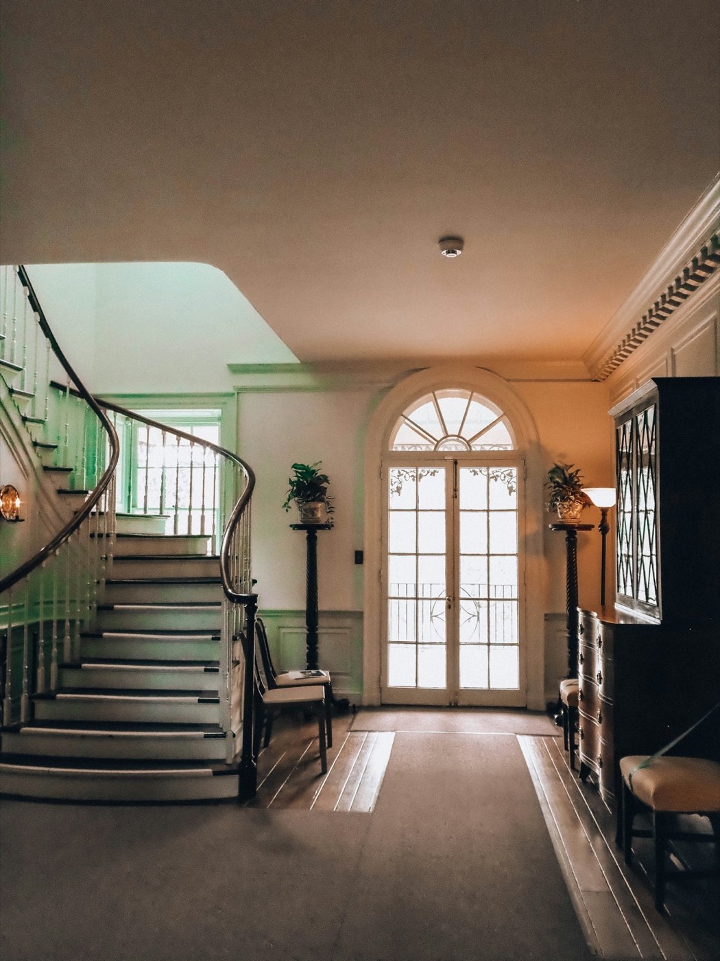 A hallway with a curving staircase and an arched window
