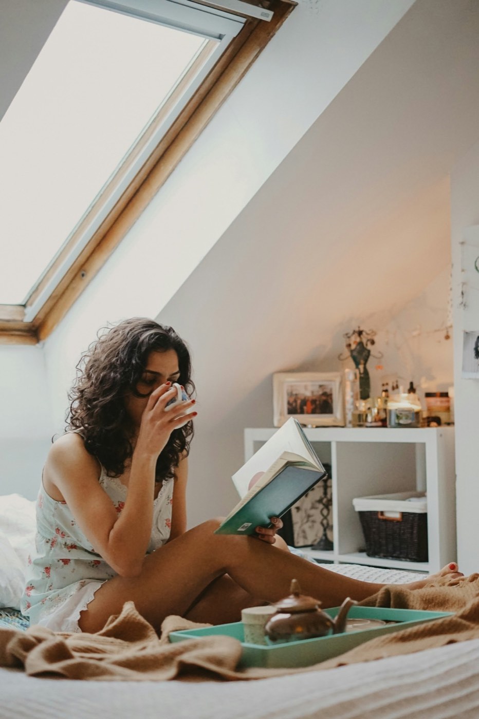 A woman sitting by a window with a cup, reading a message
