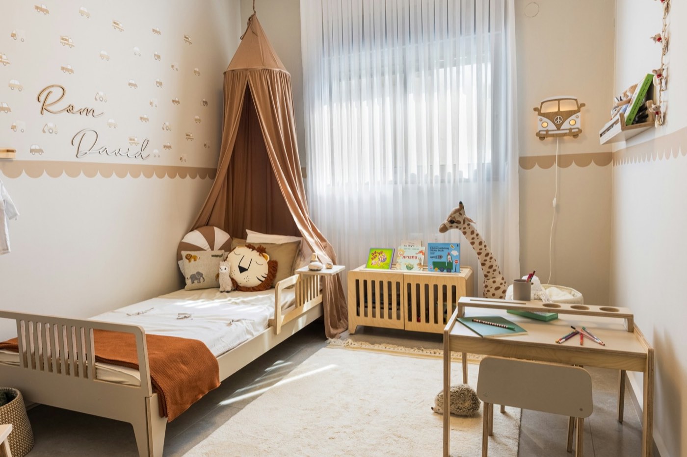 A child’s room with a low wooden bed under a fabric canopy and soft daylight